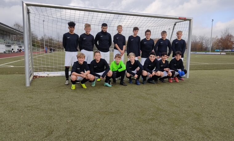 Jugendfußballmannschaft posiert vor dem Tor auf dem Spielfeld.