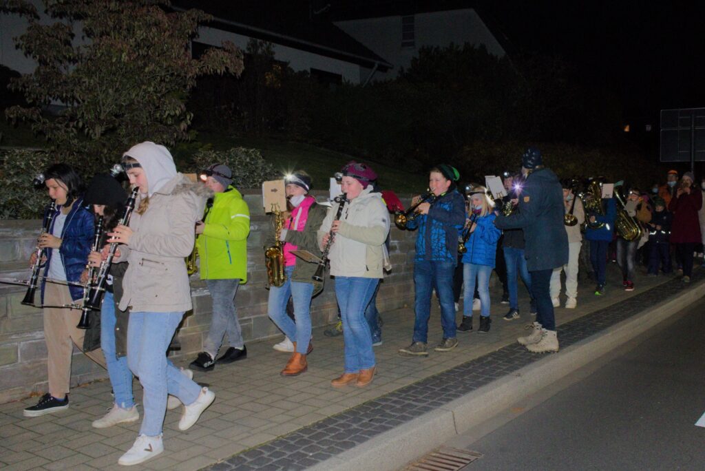 Menschen mit Instrumenten gehen nachts auf einer Straße entlang.