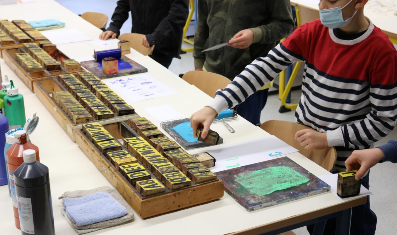 Schüler arbeiten mit Farben an Tischen in einem Kunstunterricht.
