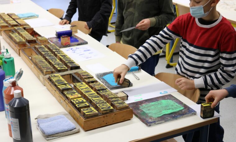 Schüler arbeiten mit Farben an Tischen in einem Kunstunterricht.