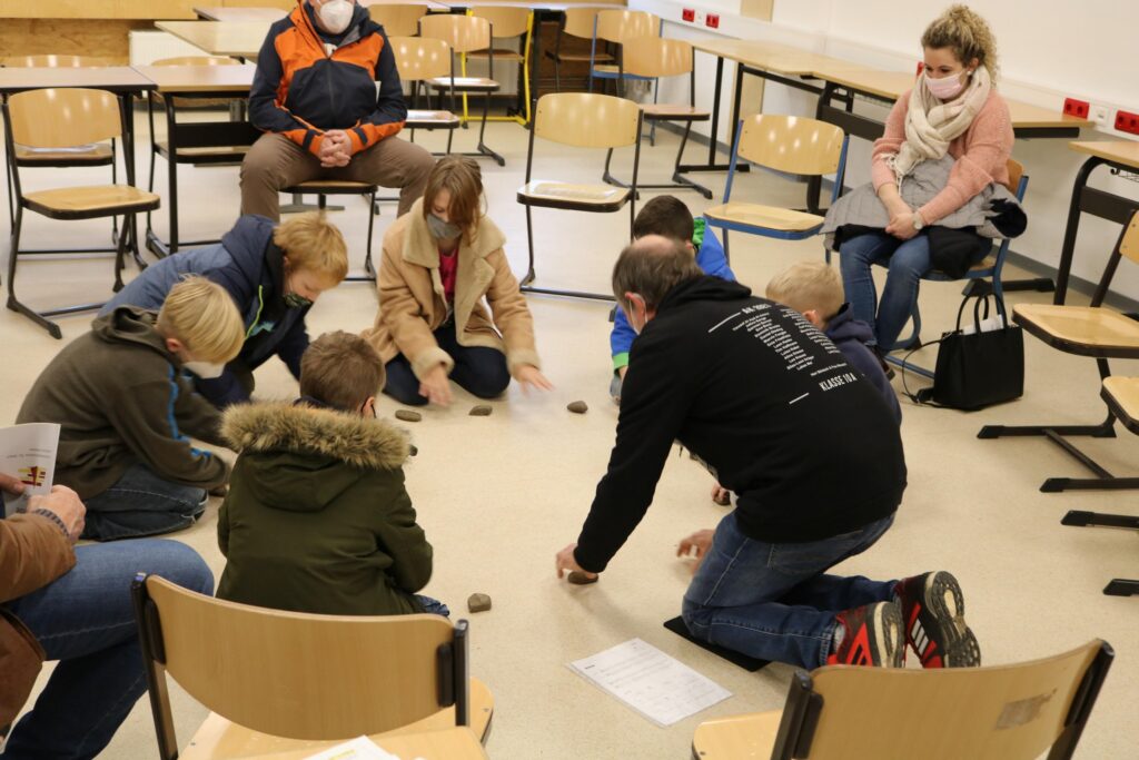 Gruppensitzung in einem Klassenraum, Teilnehmer sitzen und stehen um den Boden.