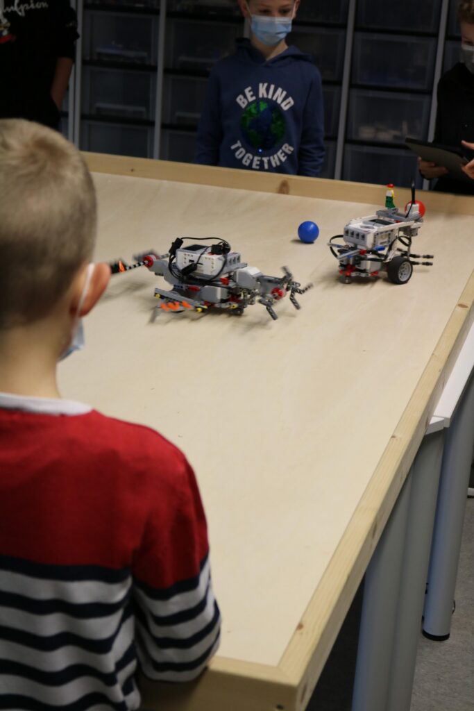 Kinder beobachten zwei Roboter auf einem Tisch.