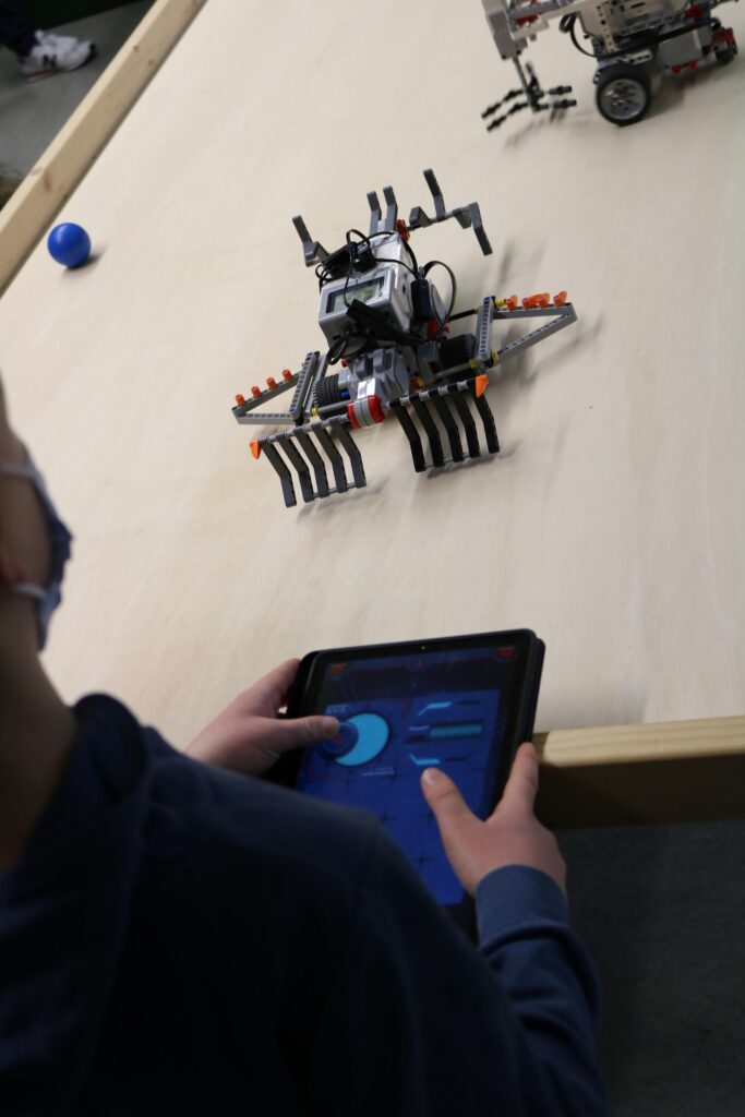 Ein Schüler steuert einen Roboter mit einem Tablet auf einem Tisch.