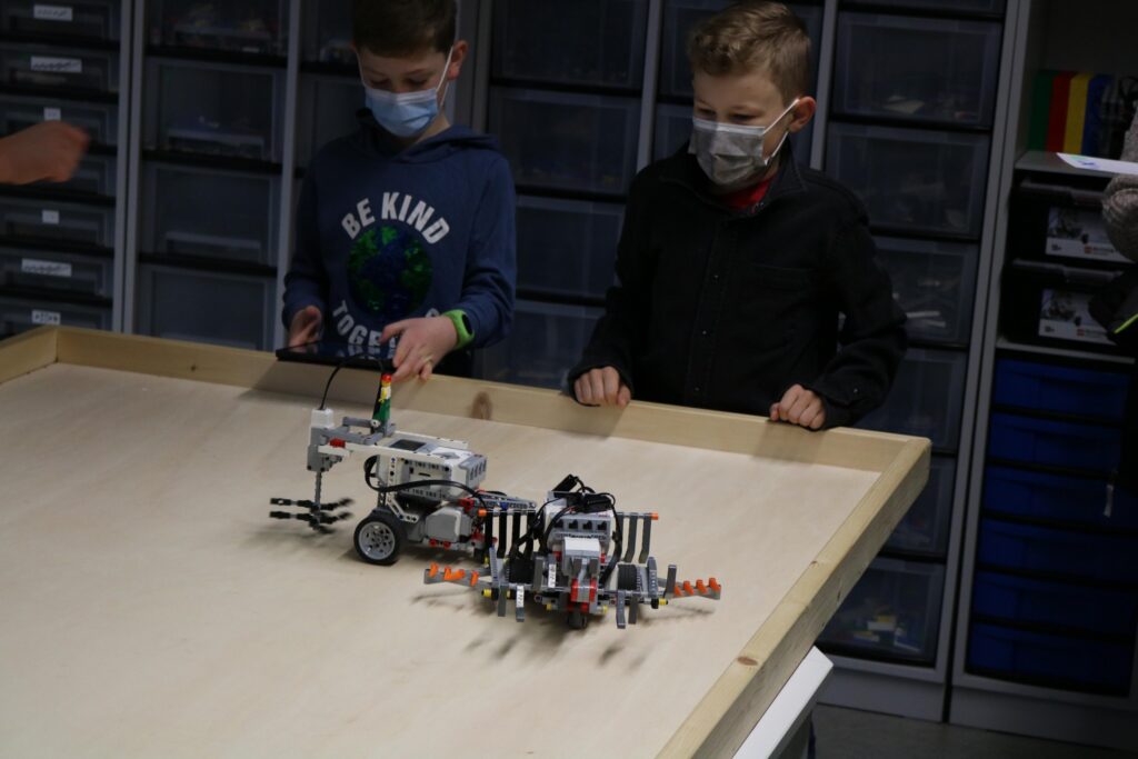 Zwei Kinder beobachten Roboter auf einem Tisch in einem Klassenraum.