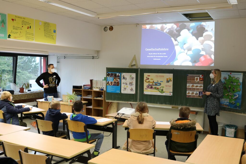Präsentation im Klassenraum mit Lehrern und Schülern am Tisch.
