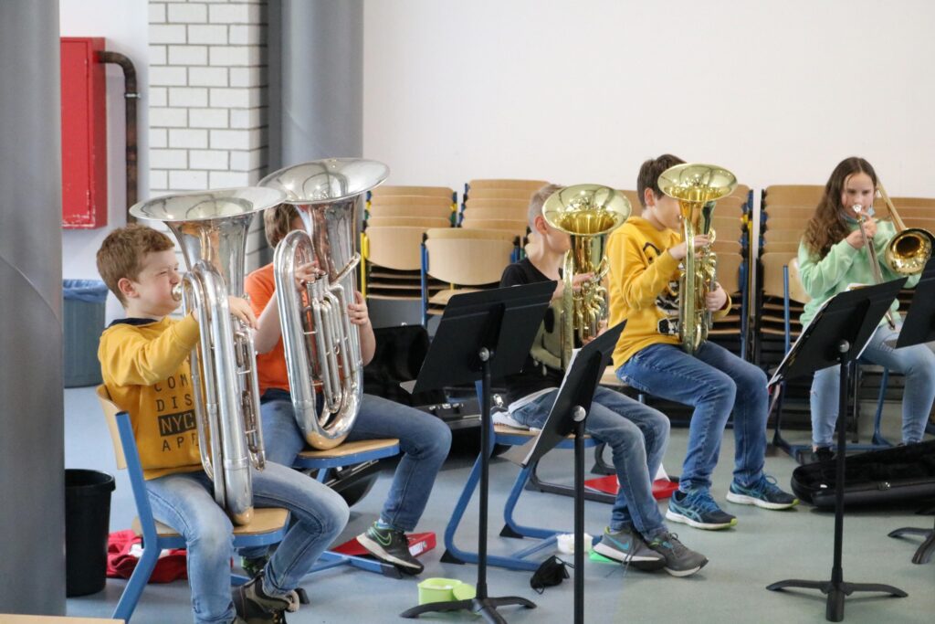 Schüler spielen gemeinsam Blechblasinstrumente in einem Probenraum.
