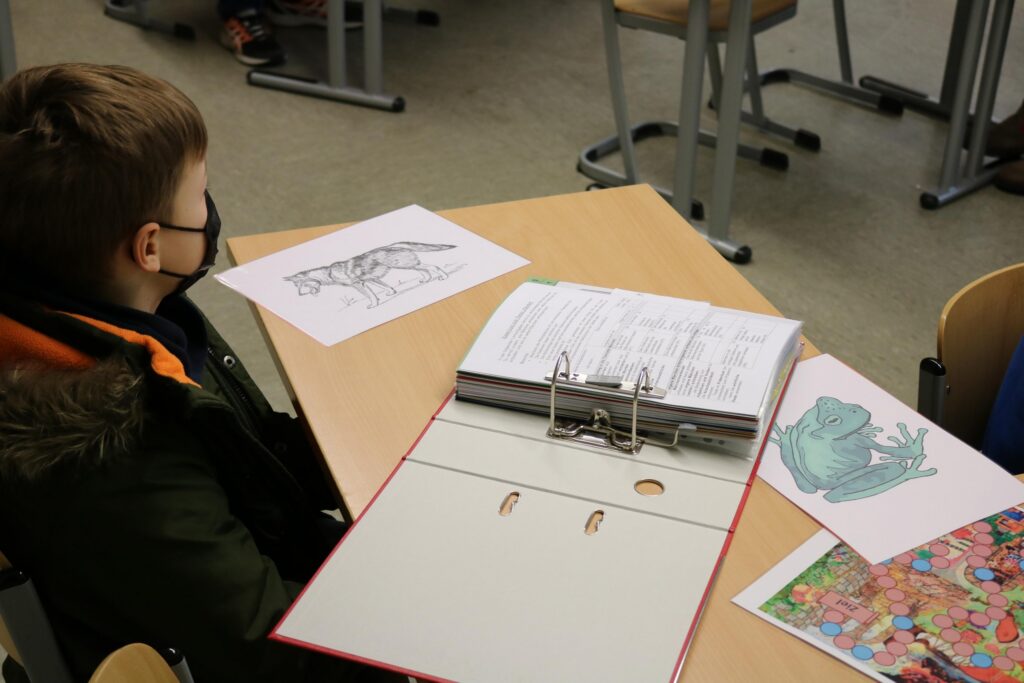 Ein Schüler sitzt an einem Tisch mit Bildern und einem Ordner.
