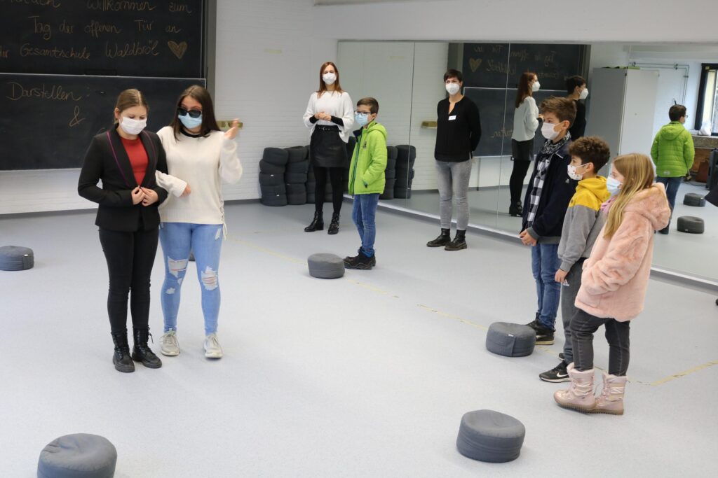 Schüler in einem Raum mit Masken, üben Gruppenaktivitäten auf runden Matten.