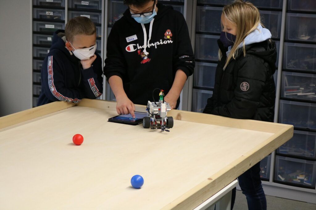 Schülerinnen und Schüler arbeiten an einem Robotermodell auf einem Tisch.