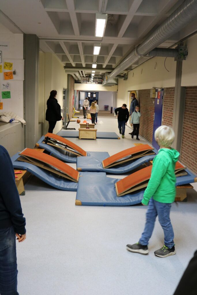 Schüler spielen im Flur mit Matten und Kästen. Einige Personen sind aktiv beteiligt.