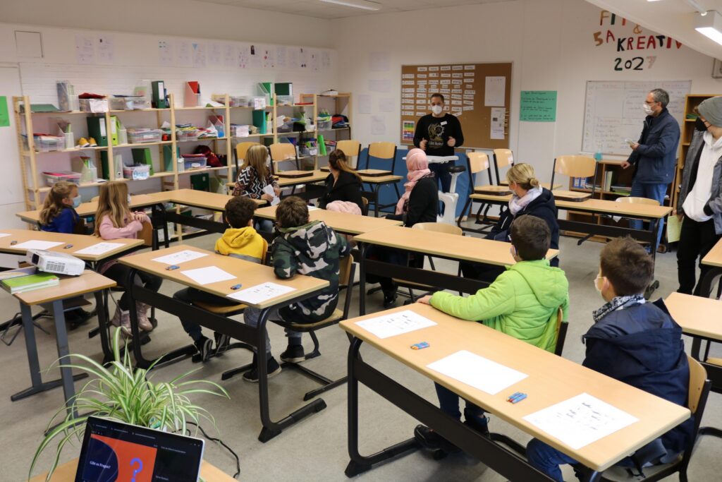 Klasse mit Schülern und Lehrern, Tische stehen in U-Form, Unterrichtssituation.