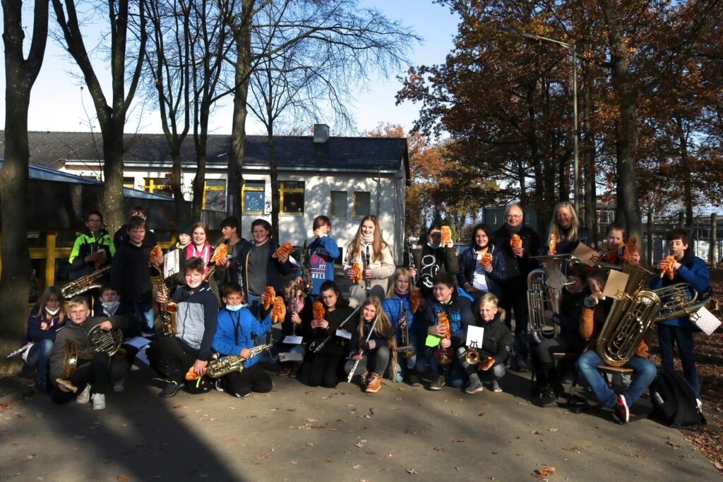 Schülerinnen und Schüler einer Blaskapelle posieren vor einem Gebäude im Freien.