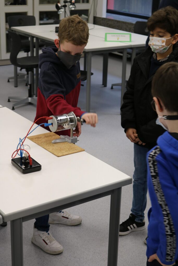 Ein Schüler demonstriert ein Experiment mit einem Motor, während andere zuschauen.
