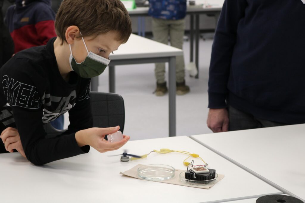 Ein Junge mit Maske beobachtet ein Experiment auf einem Tisch.