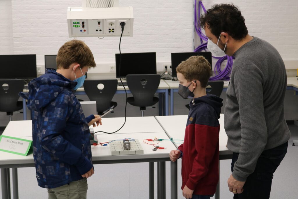 Zwei Schüler und ein Lehrer arbeiten an einem Tisch mit technischen Geräten.