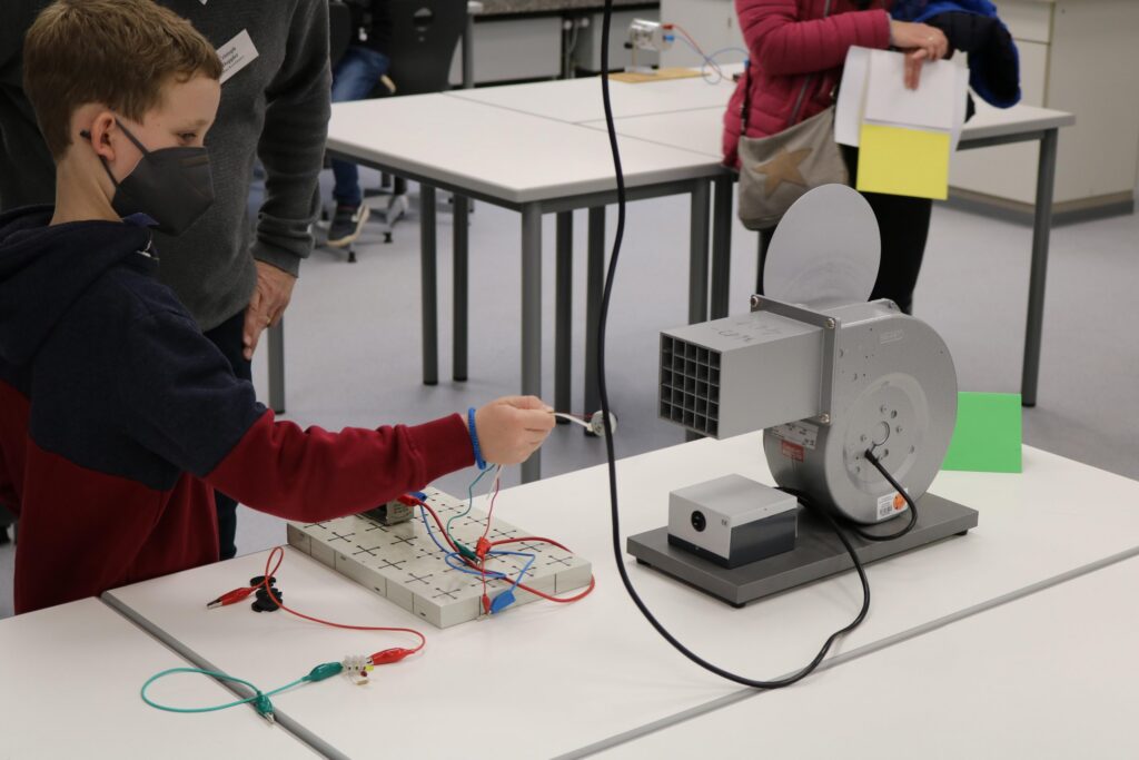 Schüler arbeitet mit einem Experimentiergerät und Kabeln an einem Tisch.