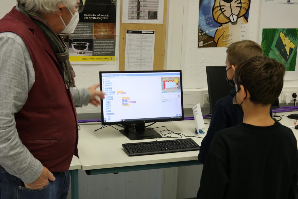 Ein Lehrer zeigt zwei Schülern etwas am Computer.