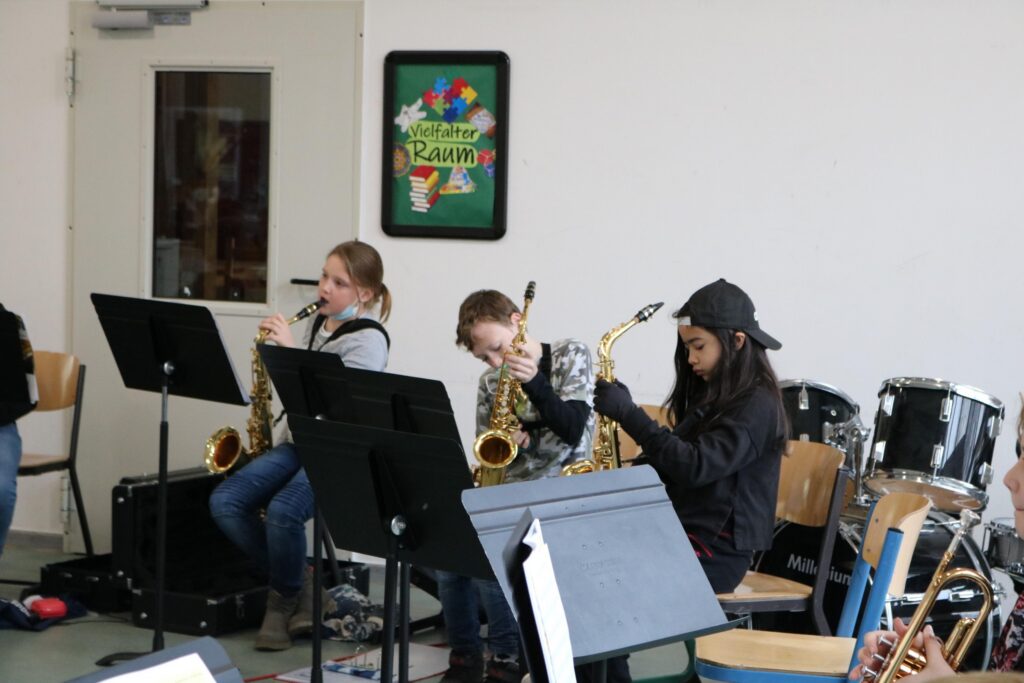 Schüler spielen Saxophon in einem Musikraum. Drums im Hintergrund sichtbar.