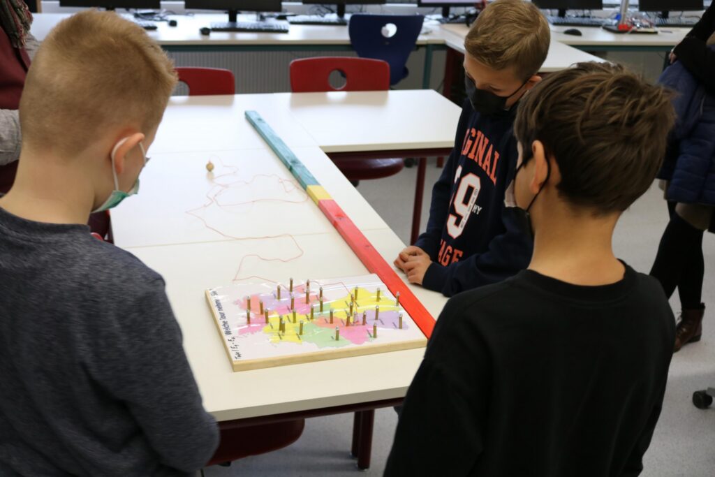 Kinder stehen um einen Tisch und spielen ein Brettspiel mit bunten Figuren.