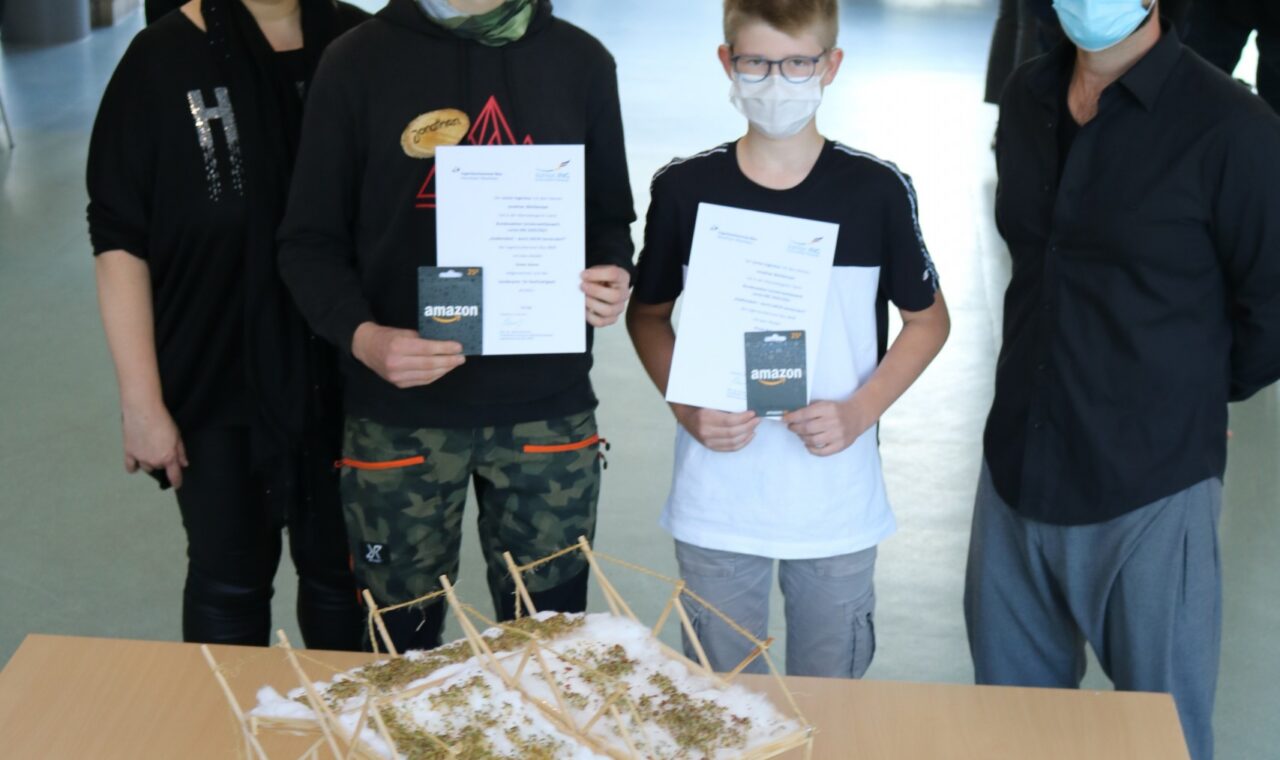 Gruppe von Personen präsentiert ein Modell auf einem Tisch. Alle tragen Masken.