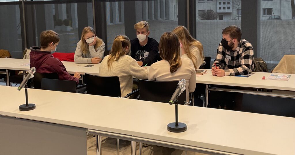 Sechs Schülerinnen und Schüler sitzen an einem Tisch und diskutieren.