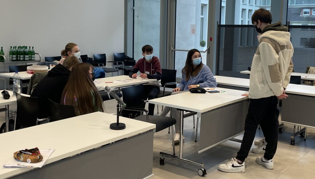 Schüler und Lehrkräfte sitzen in einem Klassenzimmer und interagieren.