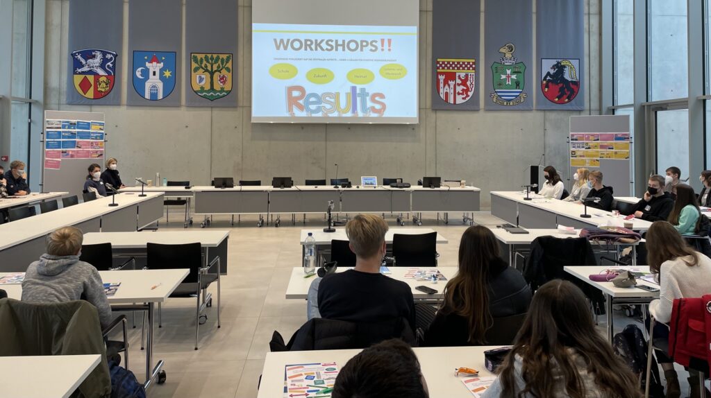 Ein moderner Raum mit Tischen, einer Präsentation und Teilnehmern bei einem Workshop.