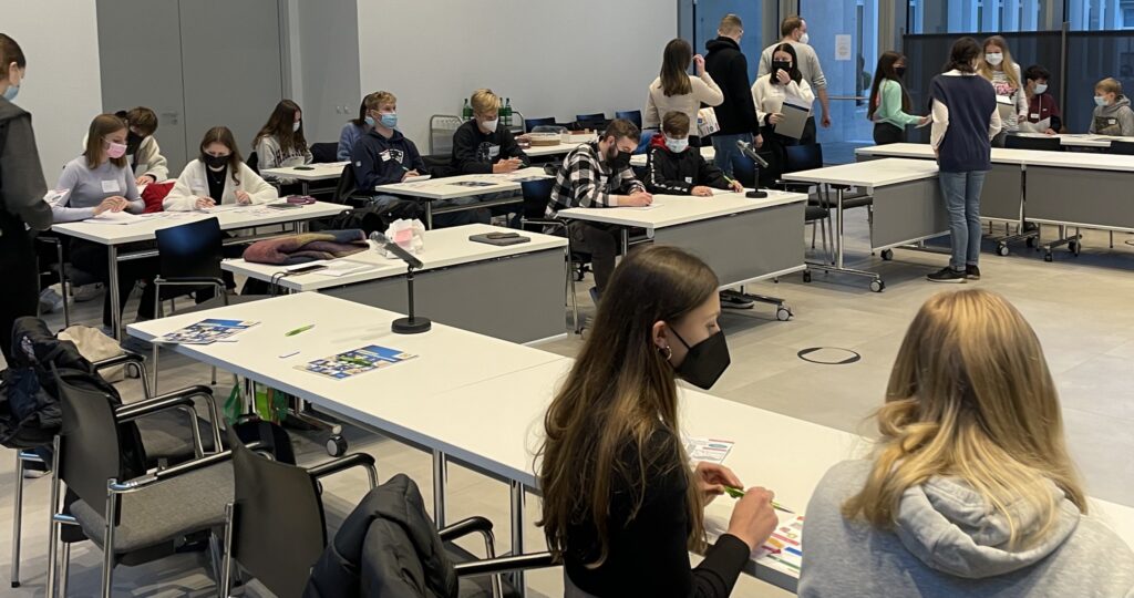 Schülerinnen und Schüler sitzen in einem Klassenraum und arbeiten an Tischen.