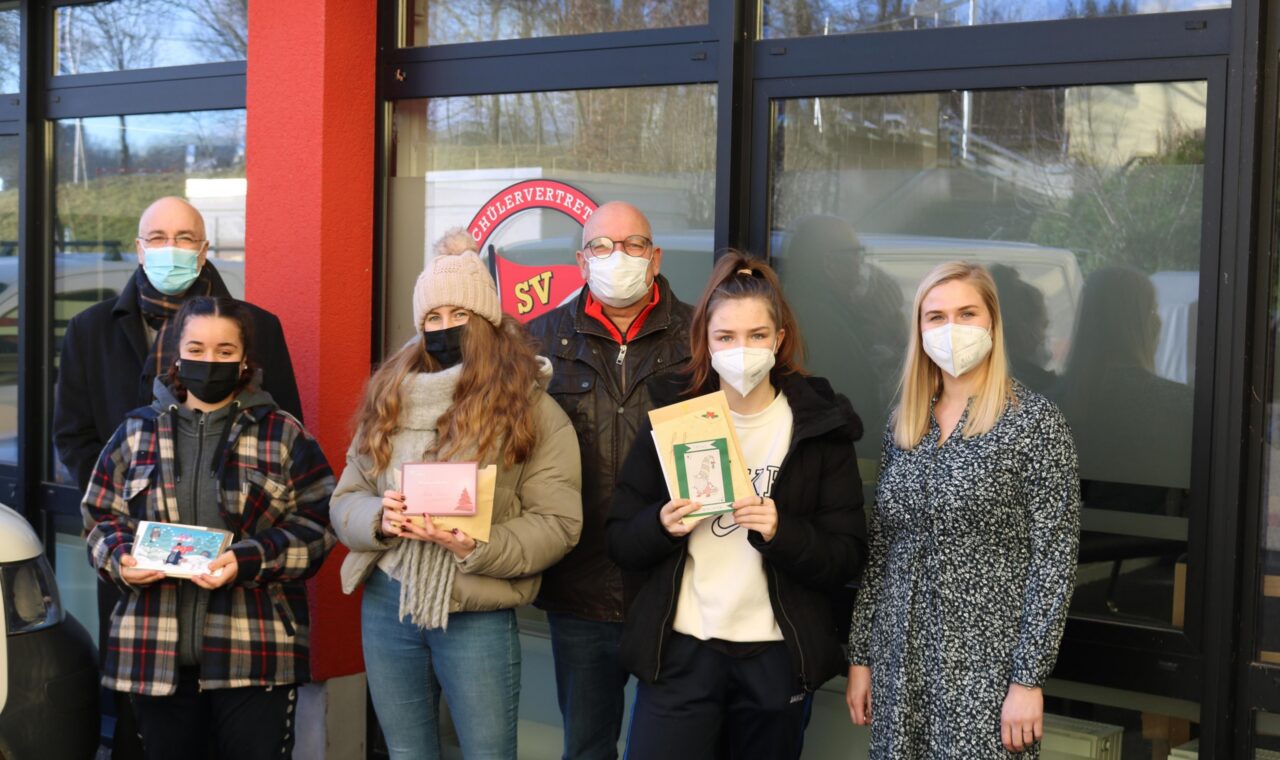 Gruppe von Schülern mit ihren Preisen vor der Schulwand. Alle tragen Masken.