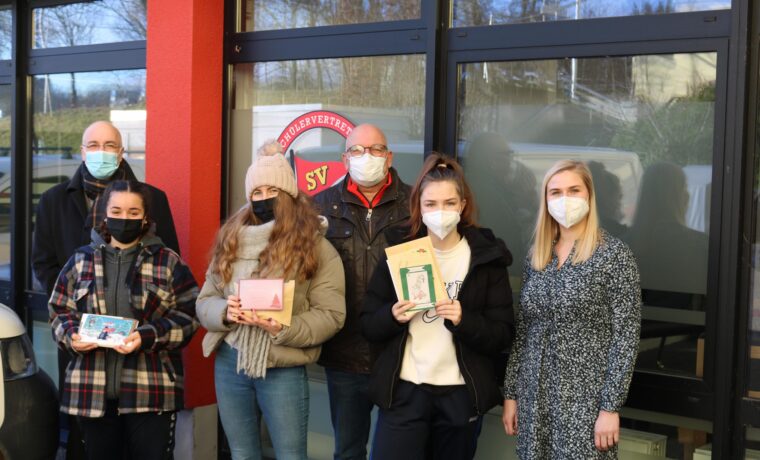 Gruppe von Schülern mit ihren Preisen vor der Schulwand. Alle tragen Masken.