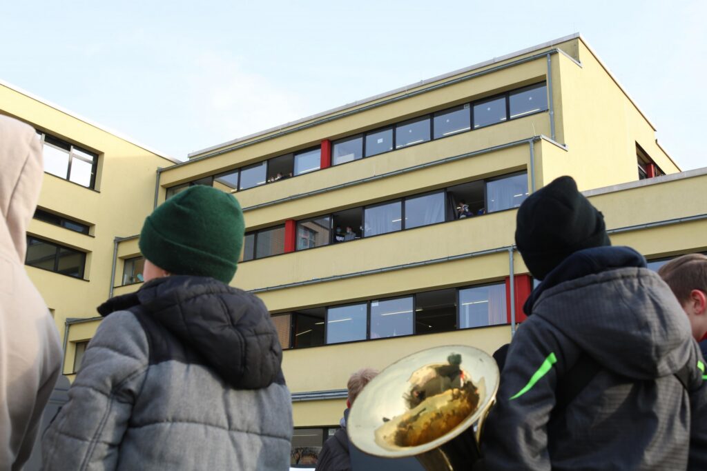 Schüler stehen vor einem Gebäude mit Fenstern und roten Vorhängen.
