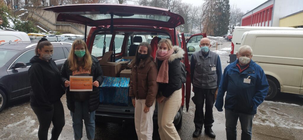 Gruppe von Personen neben einem Fahrzeug mit Spenden und Masken im Freien.
