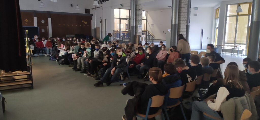 Viele Schüler sitzen in einem Veranstaltungsraum und schauen nach vorne.