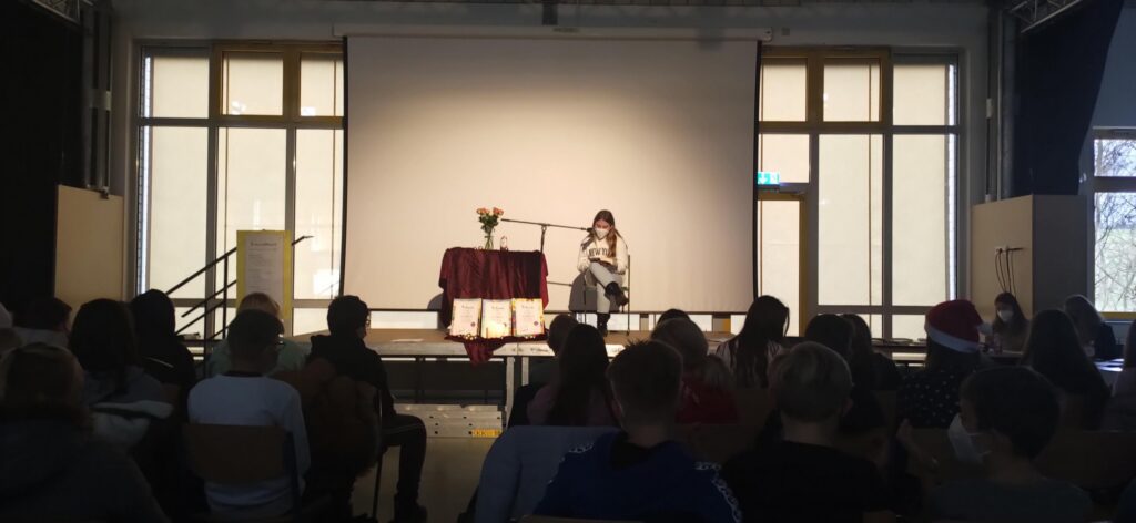 Schülerin präsentiert vor Publikum auf Bühne. Bühne ist dekoriert.