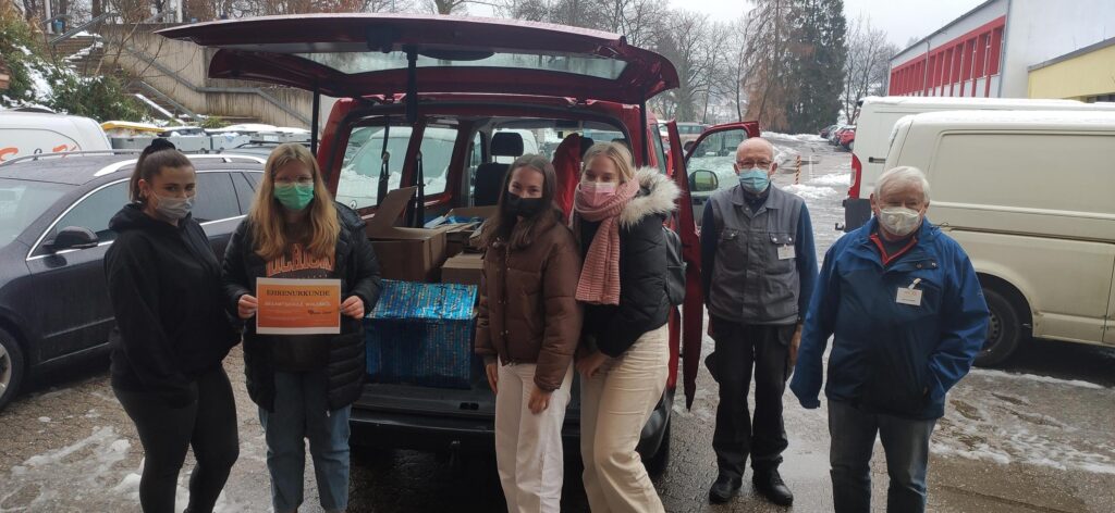 Personen stehen vor einem Auto mit Lebensmittelspenden im Kofferraum.