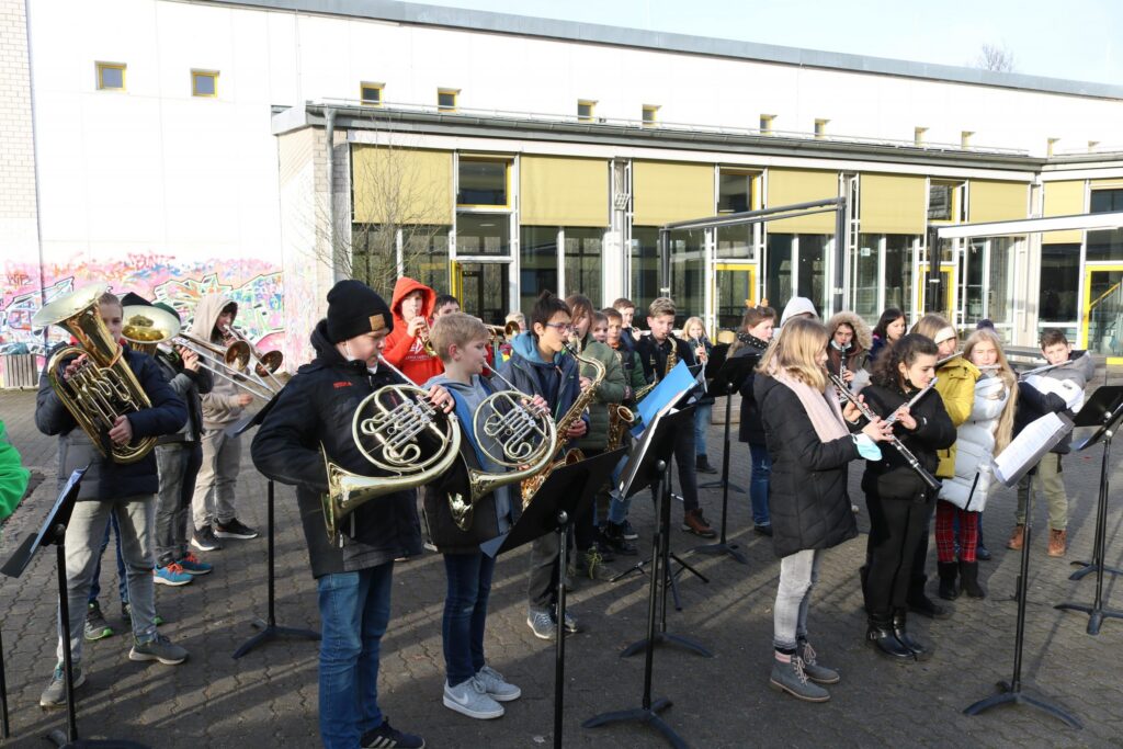Schüler der Bläserklasse spielen im Freien vor einem Gebäude.