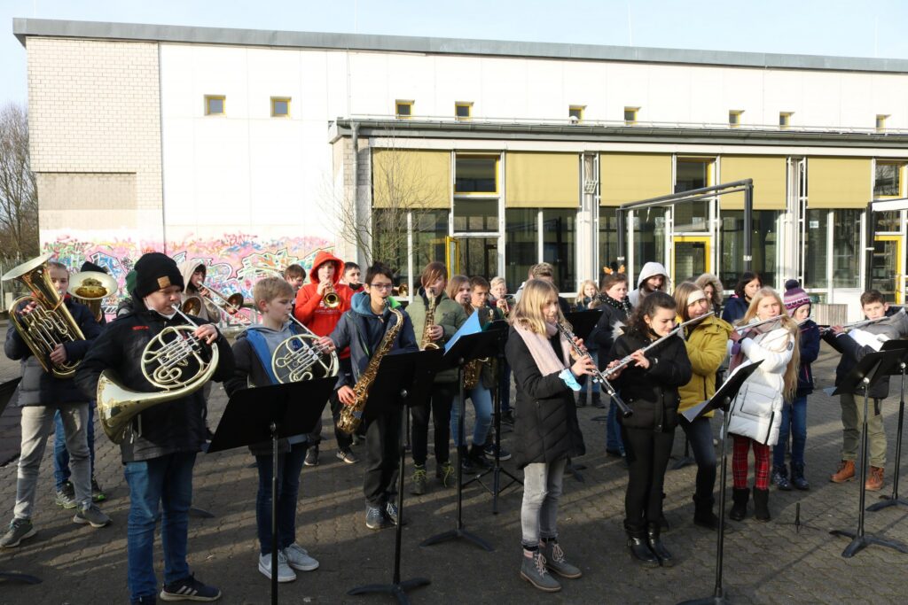 Schüler spielen ein Konzert im Freien, umgeben von Gebäuden.