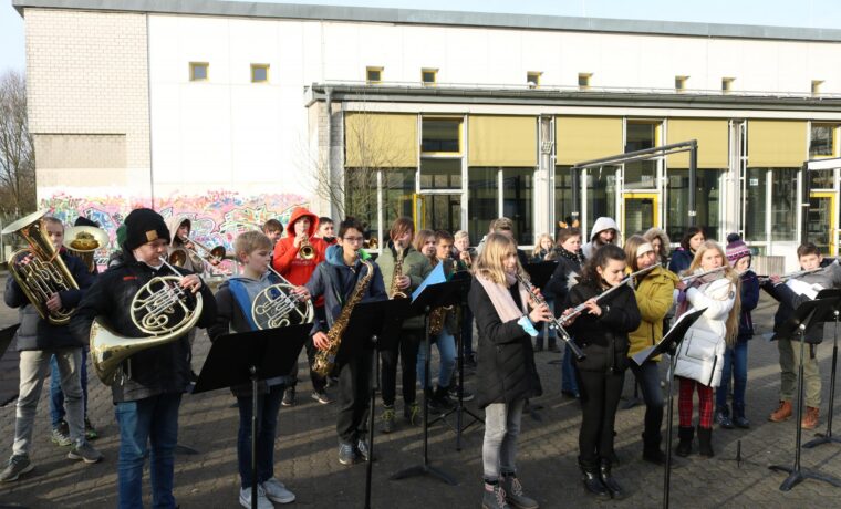 Schüler spielen ein Konzert im Freien, umgeben von Gebäuden.