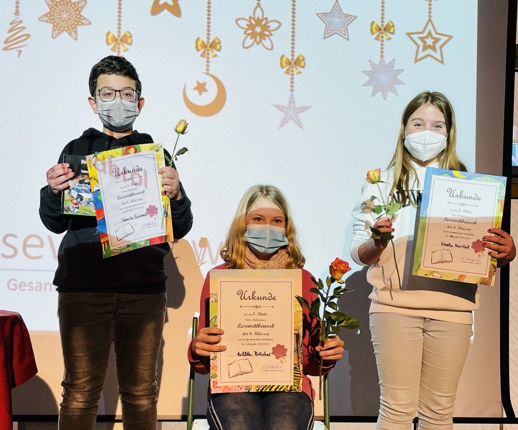 Drei Schüler halten Urkunden und Blumen in einer festlichen Umgebung.