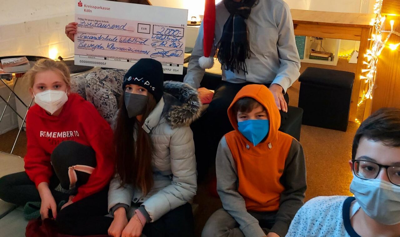 Gruppe von sechs Personen mit Masken, Weihnachtsmütze und Kerzen in einem Raum.