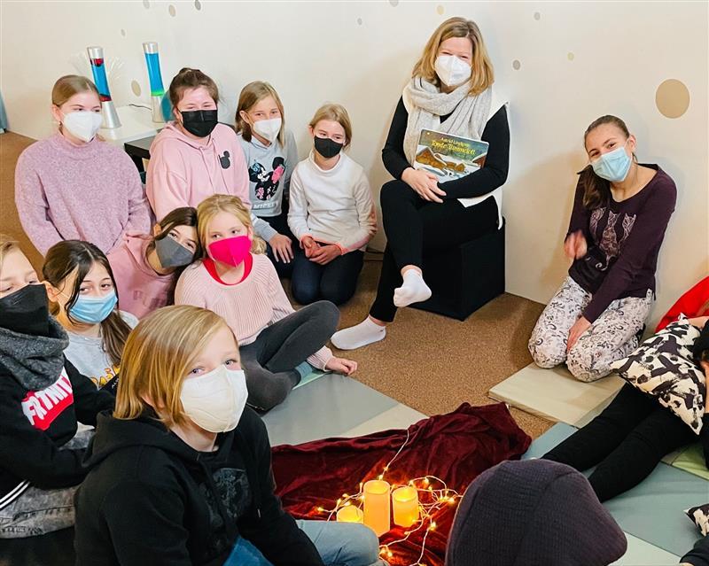 Gruppe von Schülern sitzt um ein Lichtkreis auf dem Boden, einige halten Bücher.