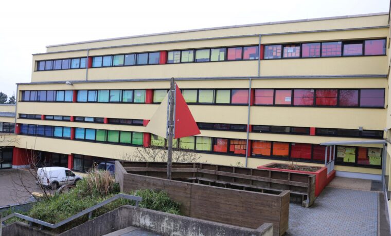 Schulgebäude mit bunten Fenstern und roter Fahne im Vordergrund.