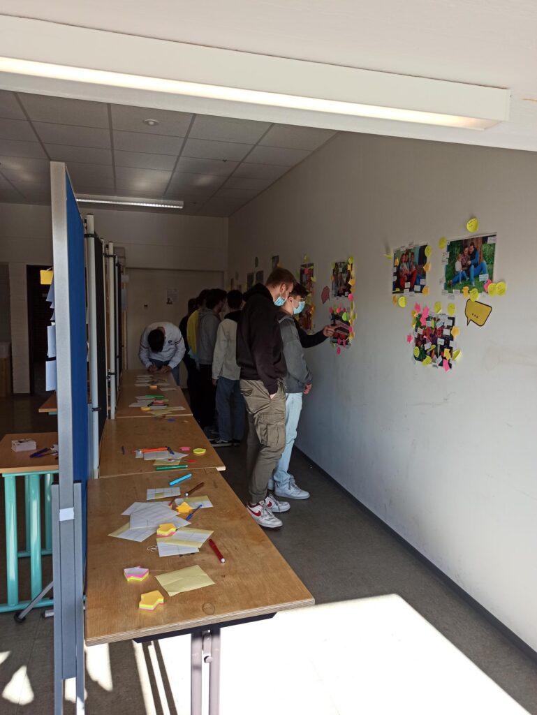 Schüler arbeiten an einer Wand mit bunten Bildern und Notizen in einem Klassenraum.