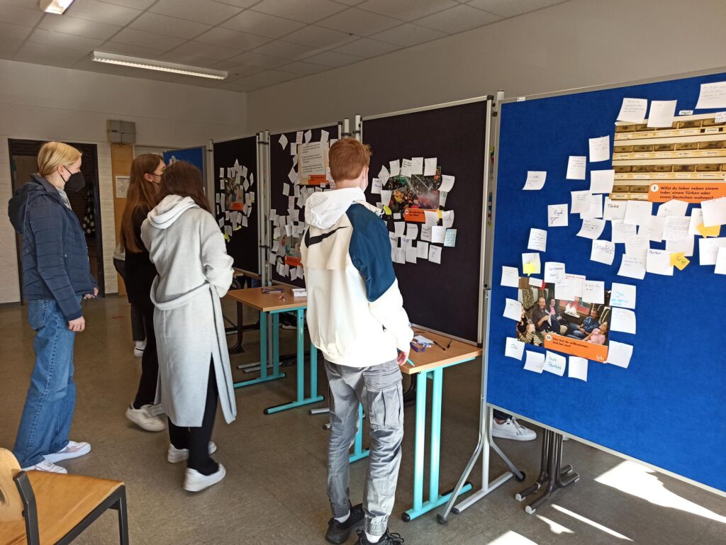 Schüler betrachten Projekte an Stellwänden in einem Klassenraum.