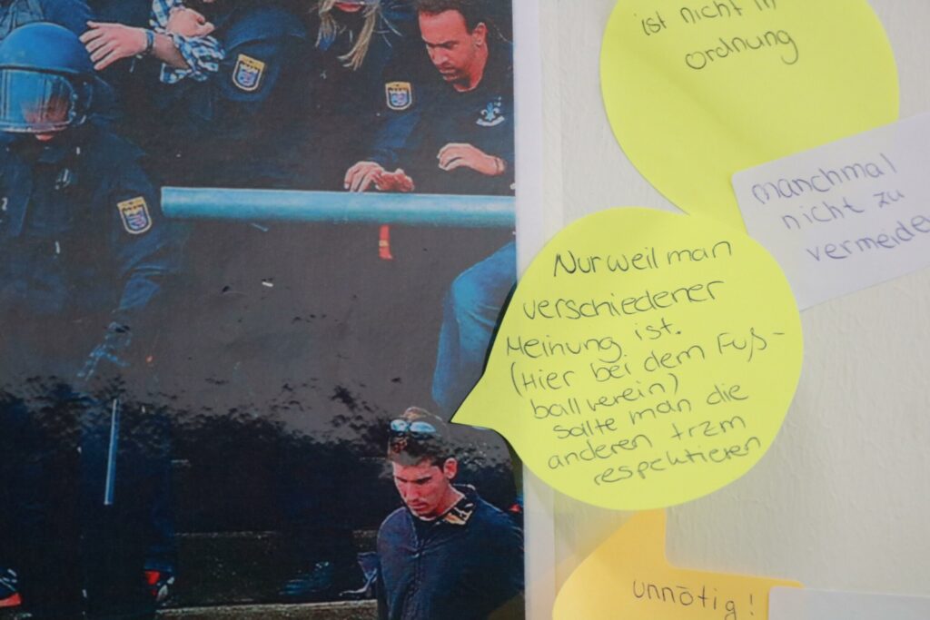 Zwei Personen in Arbeitskleidung sitzen auf einer Bank, diskutieren Notizen.