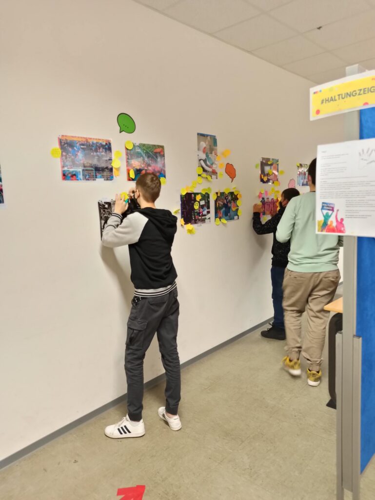 Schüler hängen Bilder an eine Wand und diskutieren dabei.