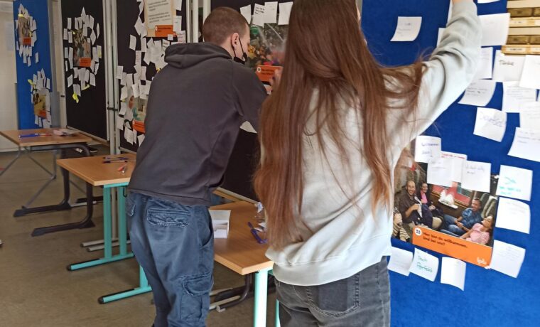 Schülerinnen und Schüler befestigen Notizen an Pinnwänden in einem Klassenraum.