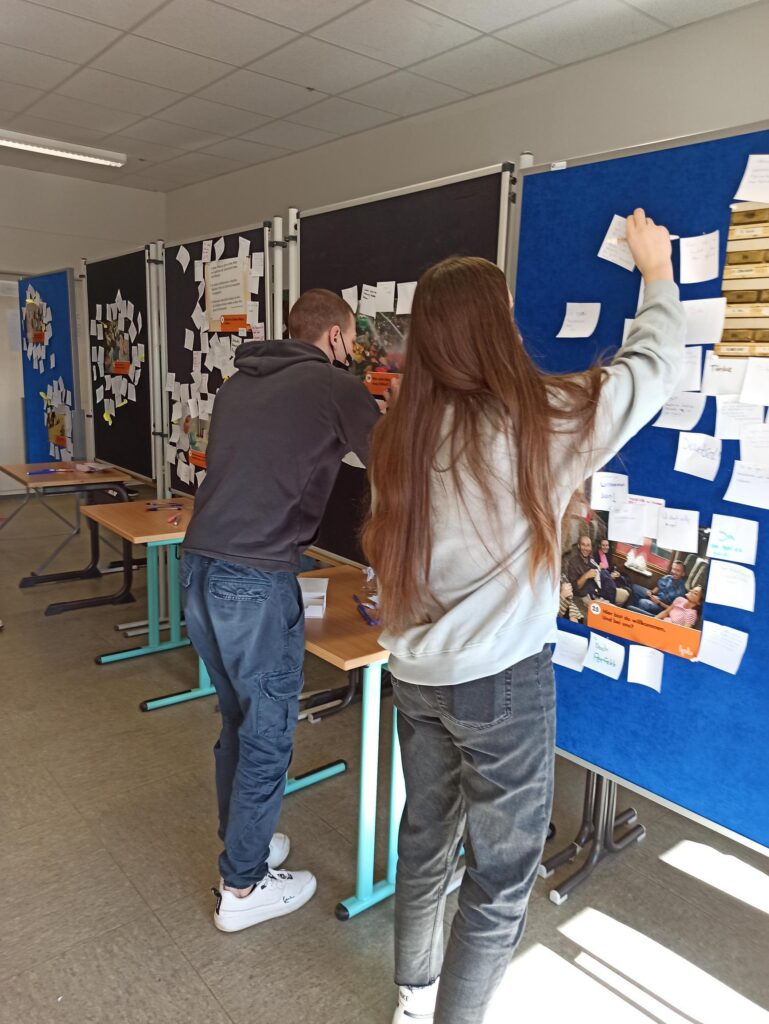 Schülerinnen und Schüler befestigen Notizen an Pinnwänden in einem Klassenraum.