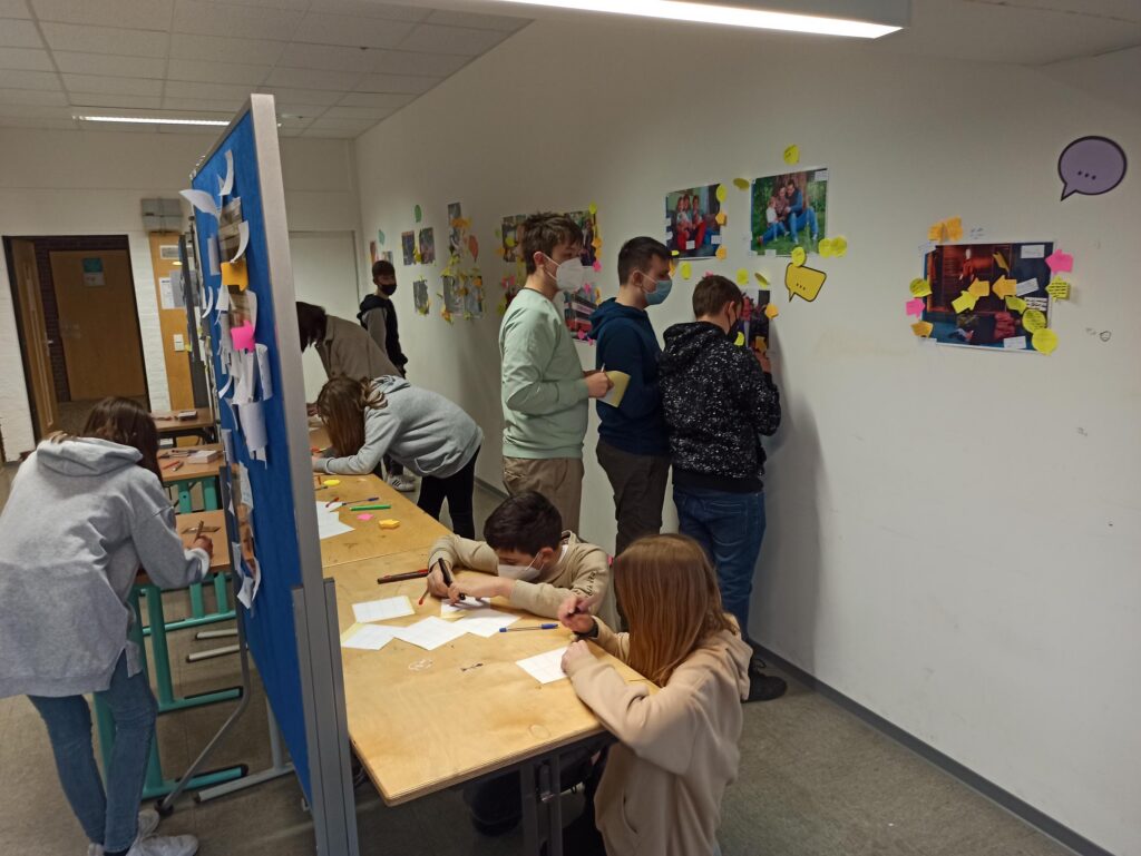 Schüler arbeiten an Tischen und gestalten Wandbilder mit bunten Notizen.
