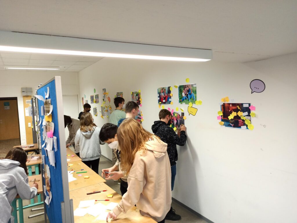 Schüler arbeiten an einem Tisch und gestalten Wände mit Bildern und Notizen.